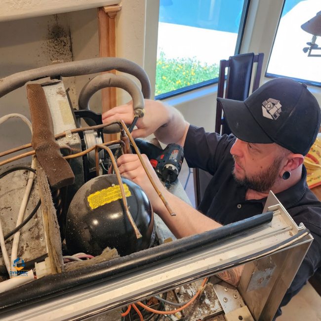 Appliance repair technician working on refrigerator compressor in Gilbert & Fountain Hills, AZ