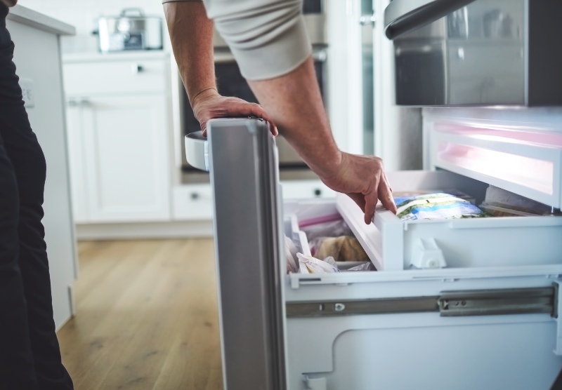 Person opening bottom freezer drawer to access frozen food for appliance repair service in Fountain Hills, AZ