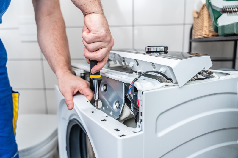 Repairman using a screwdriver disassembles a washing machine for repair in Phoenix, AZ, & surrounding areas