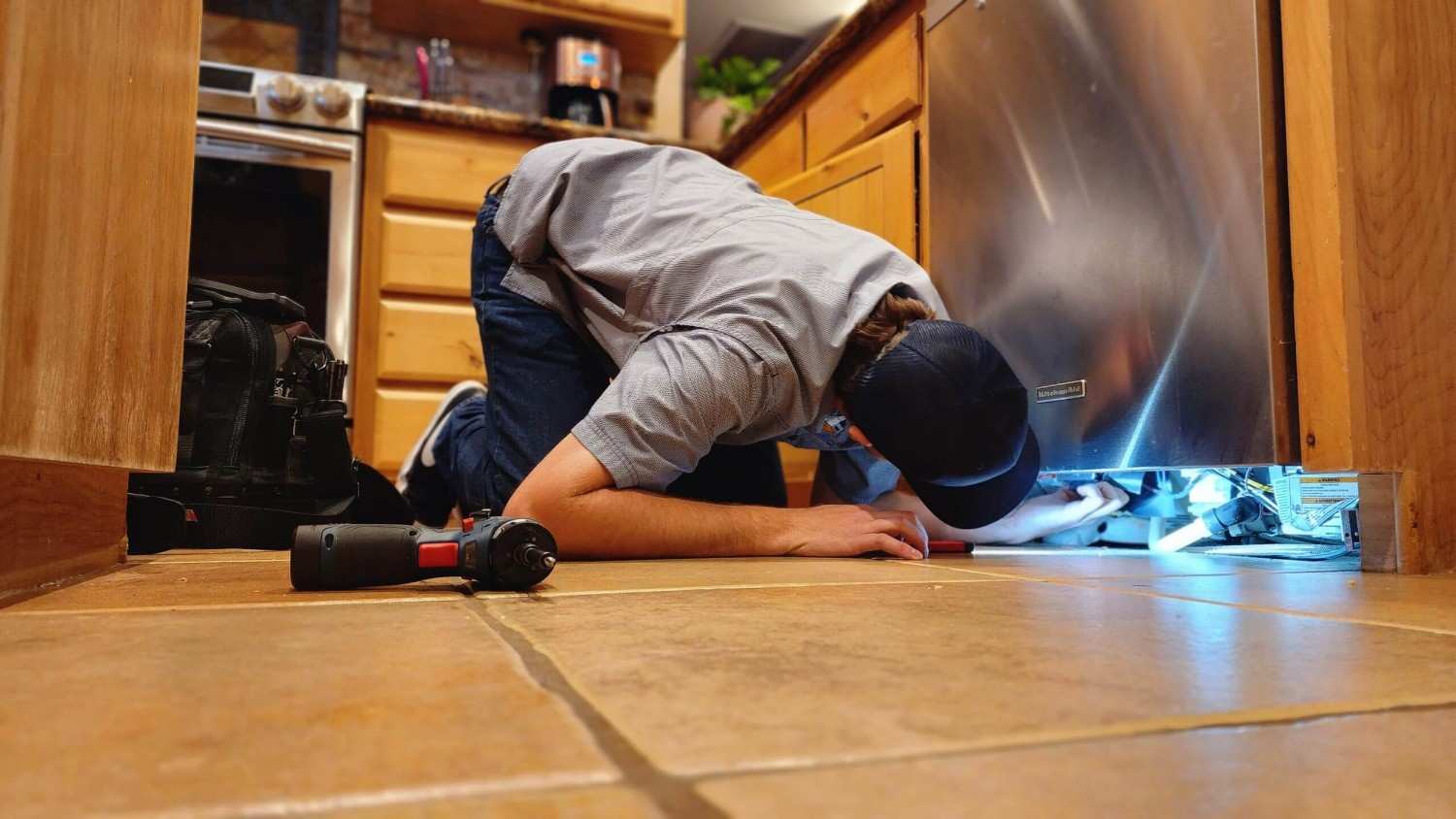 Technician inspecting dishwasher under the cabinet in Gilbert & Fountain Hills, AZ<br />

