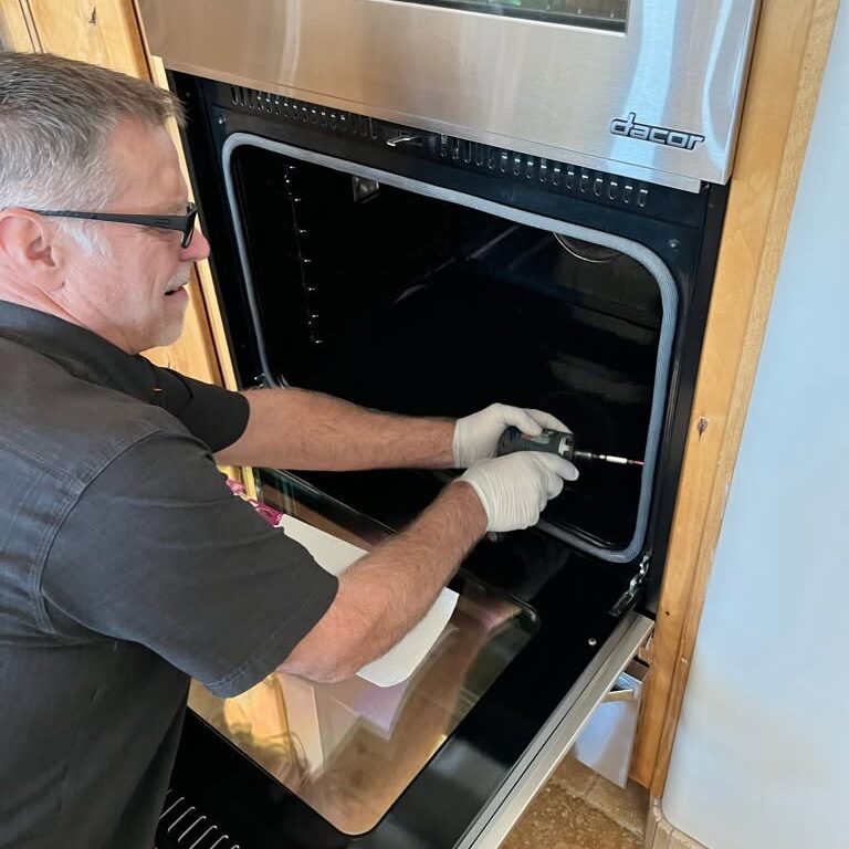 dacor oven technician Technician performing oven repair on built-in kitchen unit with tools and wiring visible
