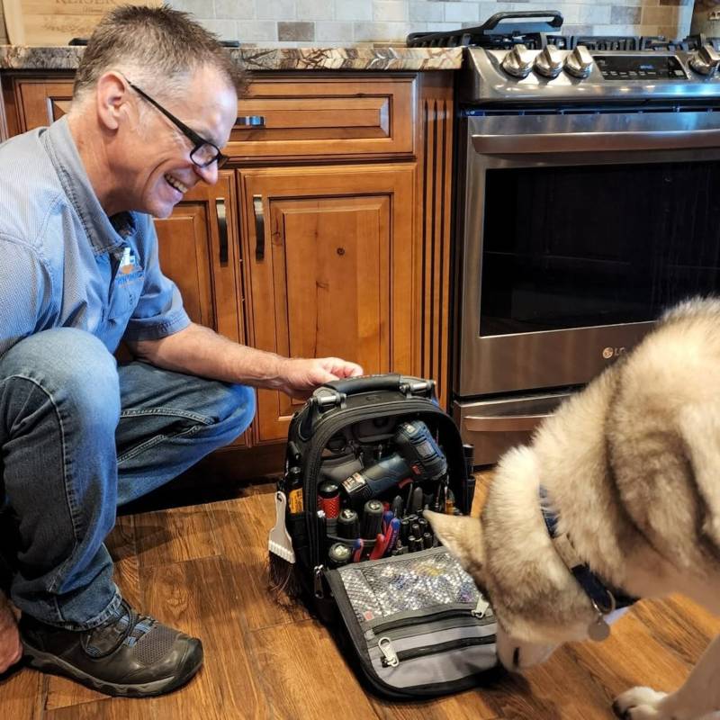Appliance technician with tool bag beside a kitchen oven and dog in Gilbert & Fountain Hills, AZ